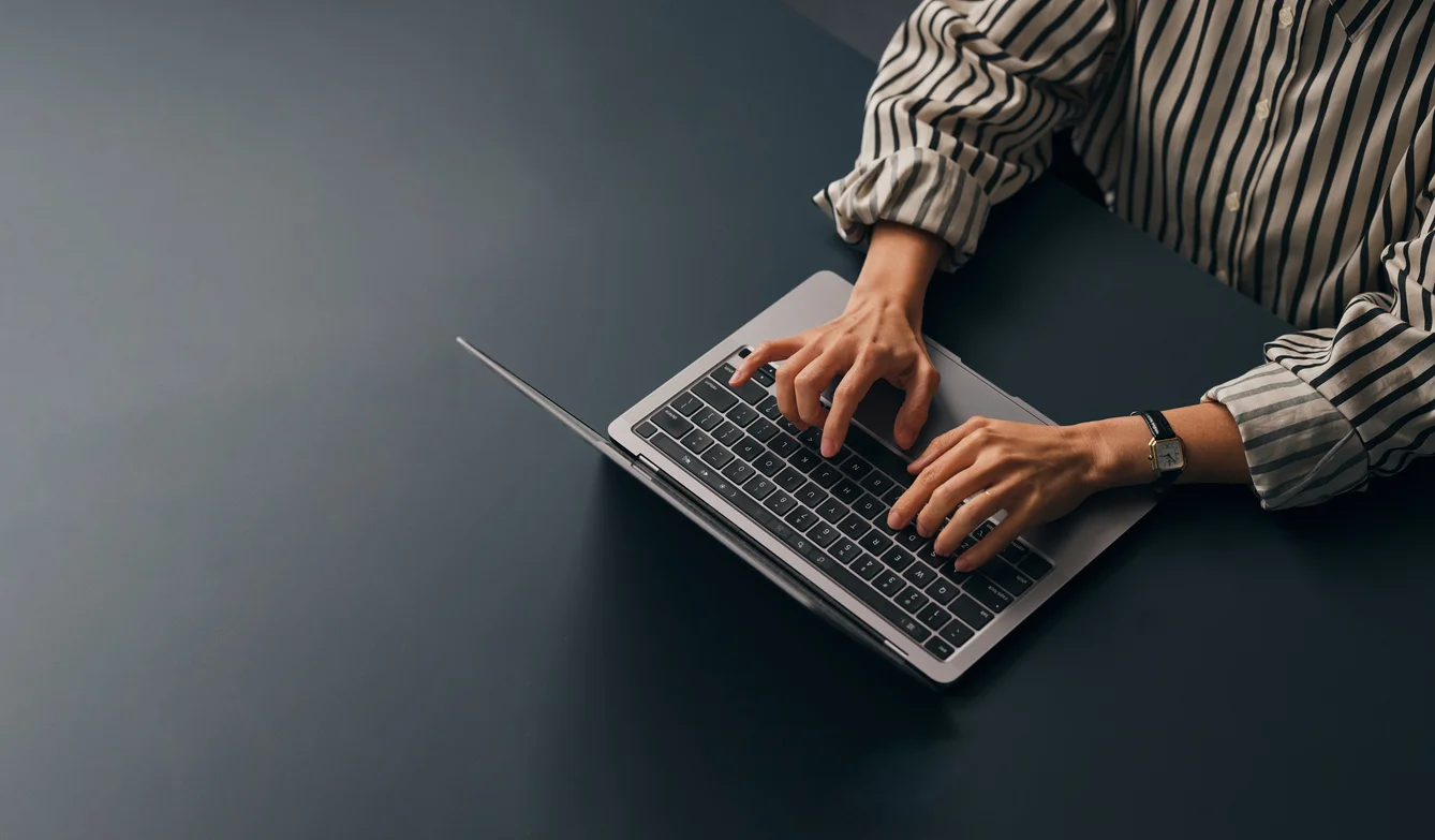 Frau in gestreifter Bluse tippt etwas auf einem Laptop